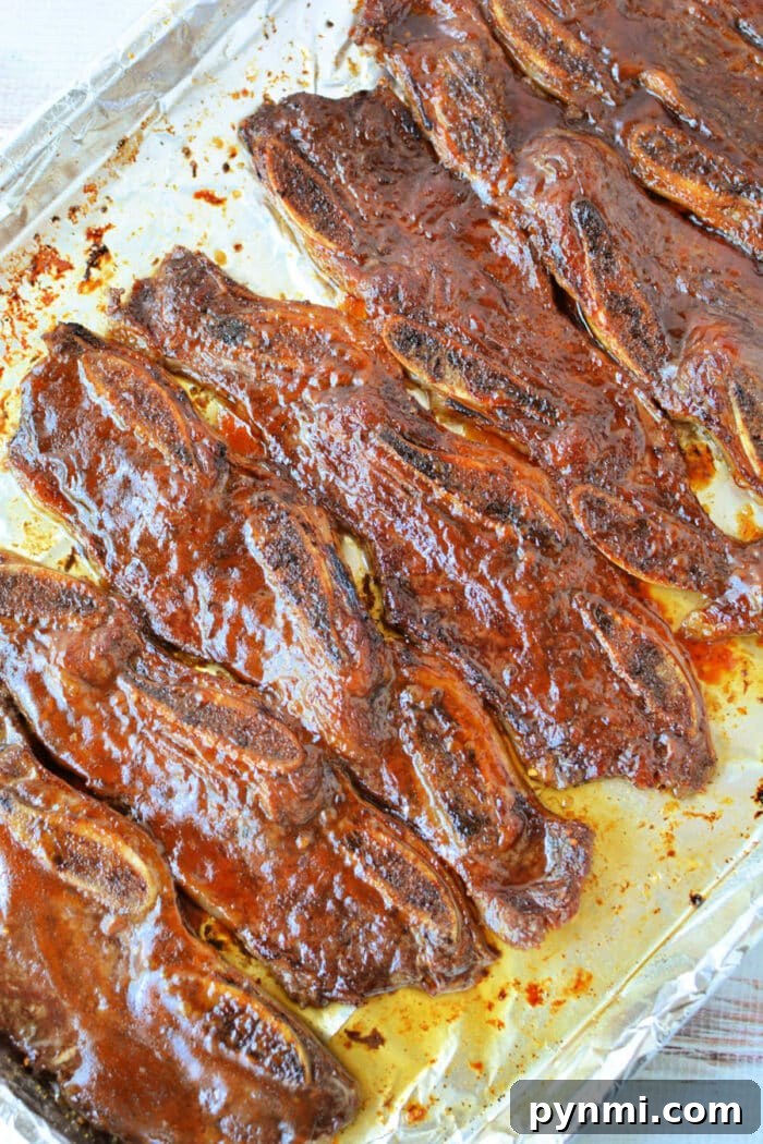 Sticky Garlic-Soy Beef Riblets with Crispy Edges 2 Rows of glazed, cooked beef riblets rest on a foil-lined baking sheet—perfect for anyone searching for a savory beef riblets recipe.