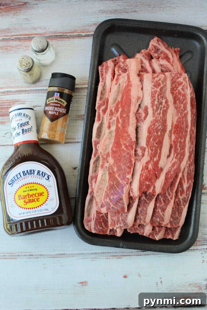 Sticky Garlic-Soy Beef Riblets with Crispy Edges 3 Raw beef riblets on a tray with barbecue sauce, smokehouse maple seasoning, salt, and pepper shakers nearby—perfect for your next beef riblets recipe.