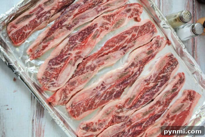 Sticky Garlic-Soy Beef Riblets with Crispy Edges 4 Raw marinated beef riblets arranged on a foil-lined baking sheet, with salt and pepper shakers nearby—perfect for trying out your favorite Beef Riblets Recipe.