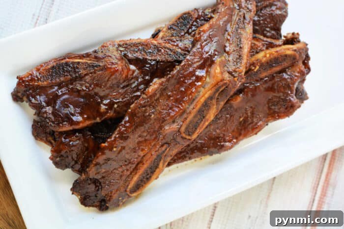Sticky Garlic-Soy Beef Riblets with Crispy Edges 6 Grilled beef riblets with a shiny glaze, served on a rectangular white plate—a mouthwatering beef recipe perfect for any occasion.