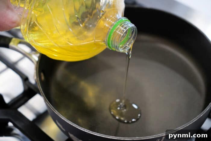 Vegetable oil being poured from a plastic bottle into a black frying pan on a stovetop, ready for preparing a delicious fried tilapia recipe.