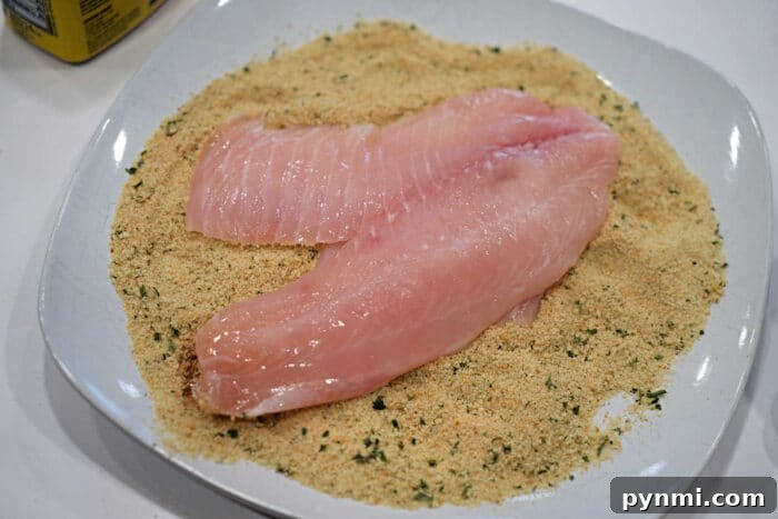 Raw fish fillets on a plate of seasoned bread crumbs, ready for coating and cooking—a classic start to any delicious Fried Tilapia recipe.