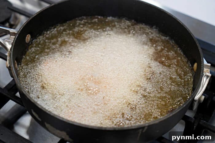 A black pan on a stove with fried tilapia deep frying in bubbling hot oil, perfect for your next tilapia recipe.