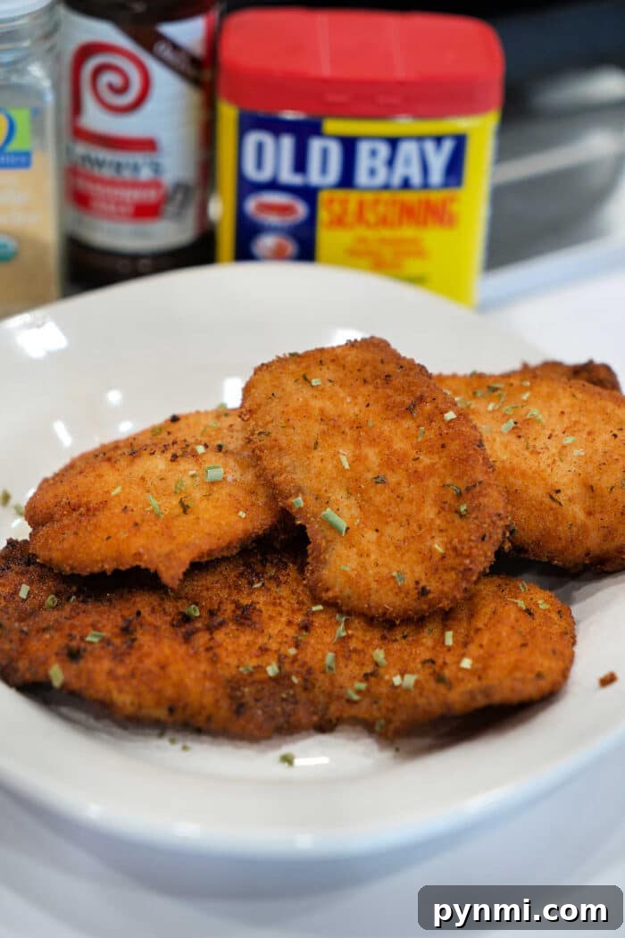 A plate of golden, breaded fried chicken cutlets, garnished with herbs, with seasoning containers behind—perfect for those who love a great Fried Tilapia or classic chicken dish.
