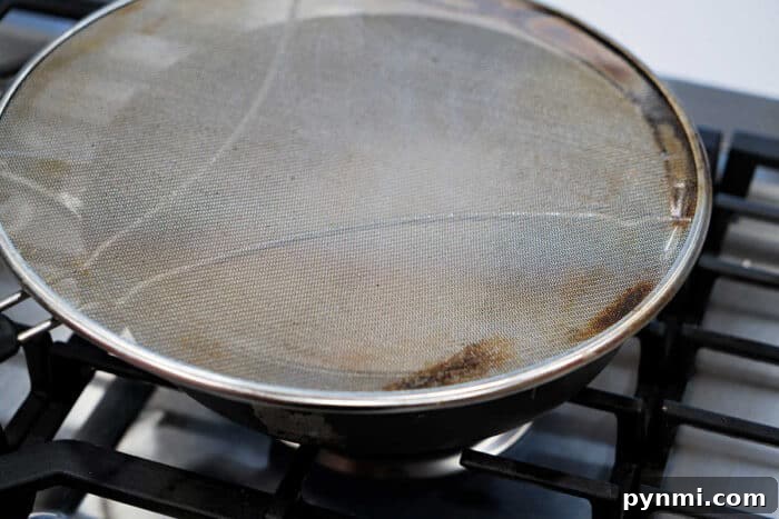 A frying pan on a stove, covered with a metal mesh splatter screen, is perfect for preparing your favorite fried tilapia recipe.