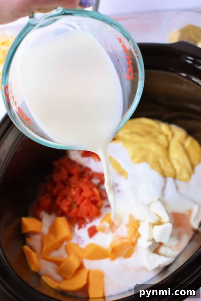 Creamy Slow-Cooker Chicken Spaghetti 4 A measuring cup pours milk into a slow cooker filled with cheese, diced tomatoes, and all the delicious ingredients needed for Crockpot Chicken Spaghetti.