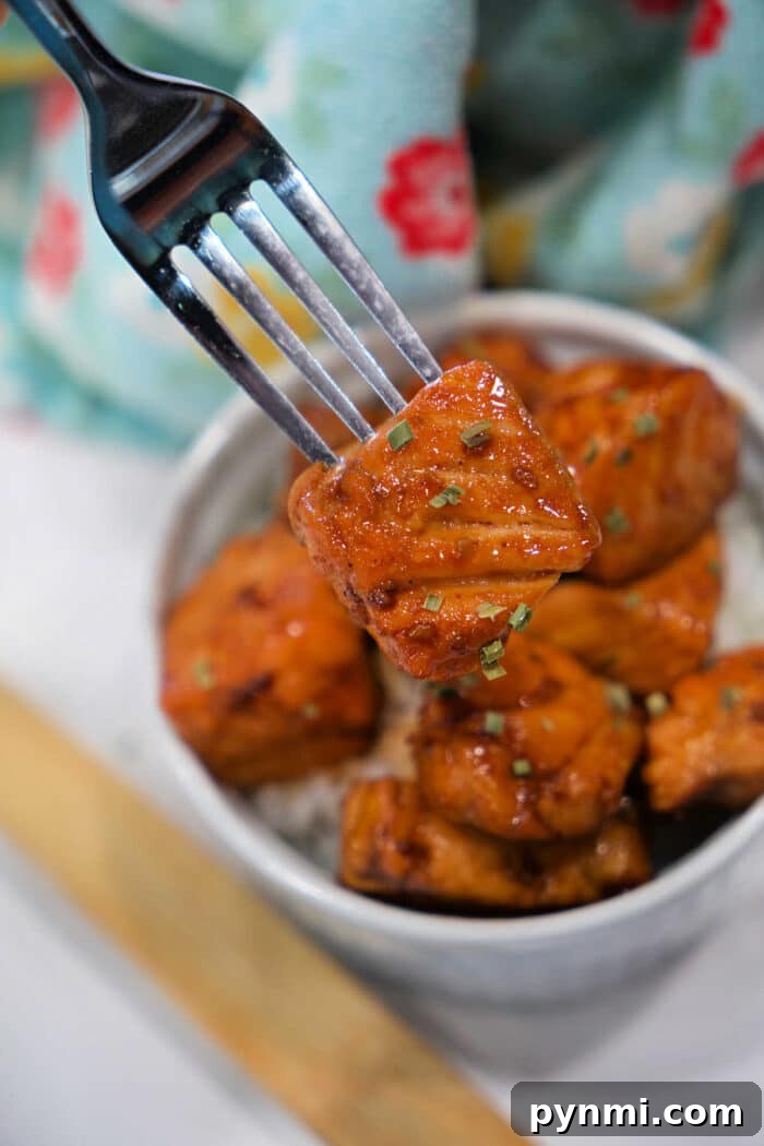 Sticky Teriyaki Salmon Bites Recipe with Sesame Glaze 2 A fork holds a piece of glazed tofu above a bowl filled with more tofu pieces and rice, offering a plant-based twist on classic Teriyaki Salmon Bites.