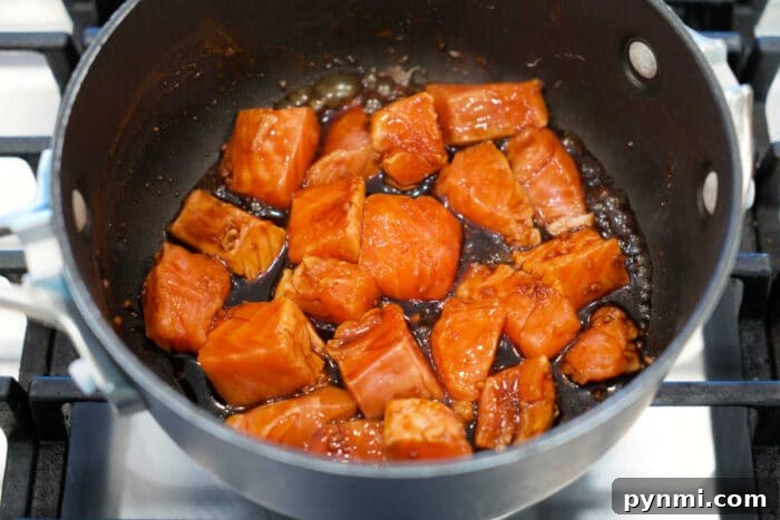 Sticky Teriyaki Salmon Bites Recipe with Sesame Glaze 5 Chunks of salmon cooking in a dark teriyaki sauce in a saucepan on a stovetop—perfect for a quick Teriyaki Salmon recipe or flavorful Salmon Bites.