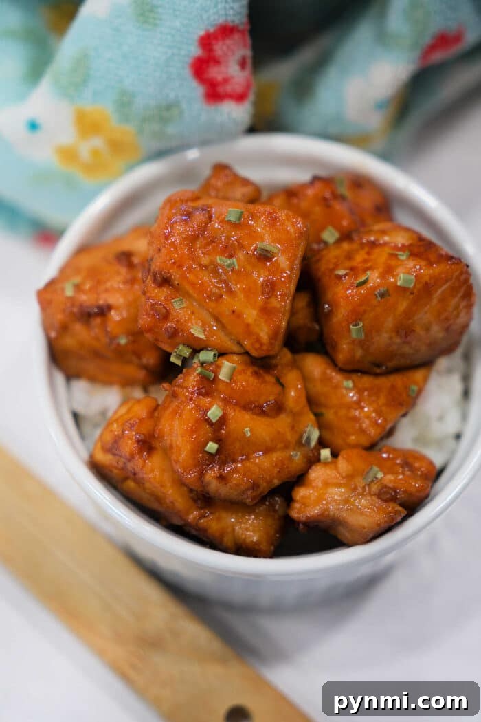 Sticky Teriyaki Salmon Bites Recipe with Sesame Glaze 7 Bowl of Teriyaki Salmon Bites on white rice, garnished with herbs, with a patterned cloth in the background.