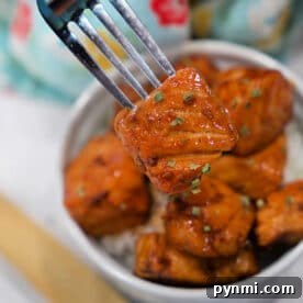 Sticky Teriyaki Salmon Bites Recipe with Sesame Glaze 8 A fork holds a piece of glazed tofu above a bowl filled with more tofu pieces and rice, offering a plant-based twist on classic Teriyaki Salmon Bites.