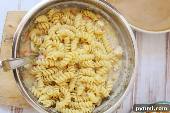 Cheesy Ritz Chicken Casserole with Crispy Cracker Topping 5 A metal bowl with rotini pasta mixed in a creamy sauce, reminiscent of the comforting flavors found in a Ritz Chicken Casserole, with a spoon inside the bowl.