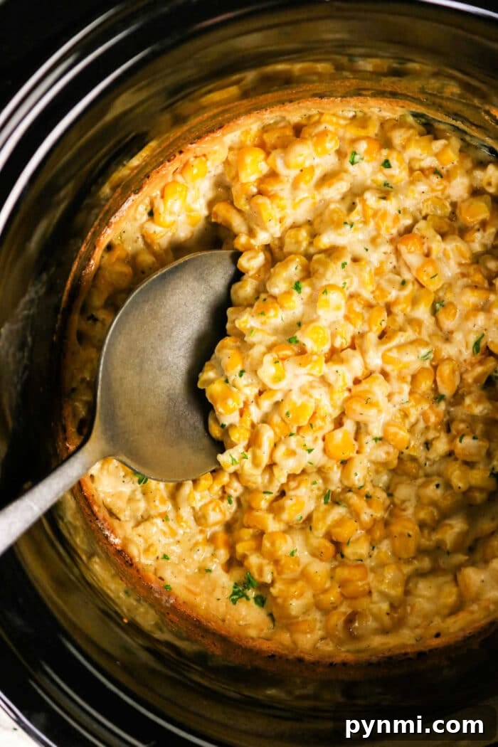 Slow Cooker Creamed Corn 6 A spoon in a Crockpot filled with creamy cooked corn, garnished with herbs—perfect for savoring delicious Crockpot Creamed Corn.