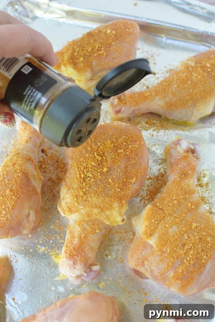 How to Bake Frozen Chicken Legs for Crispy, Juicy Results 5 A hand sprinkles seasoning onto raw chicken drumsticks on a foil-lined baking sheet, preparing them to become flavorful baked chicken legs.