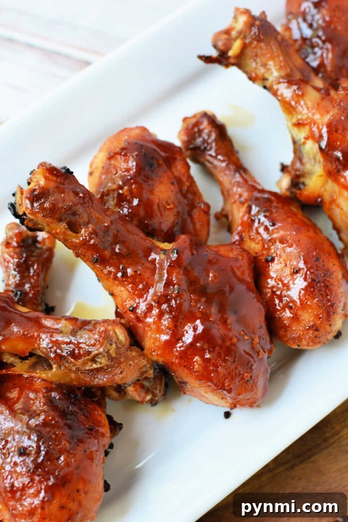 How to Bake Frozen Chicken Legs for Crispy, Juicy Results 6 Baked frozen chicken drumsticks, glazed with barbecue sauce, are arranged on a white rectangular plate.