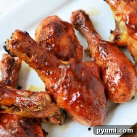 Baked frozen chicken drumsticks, glazed with barbecue sauce, are arranged on a white rectangular plate.