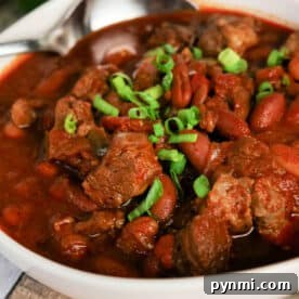 Bowl of hearty Chuck Roast Chili with beef, beans, and chopped green onions, with a spoon resting in the bowl.